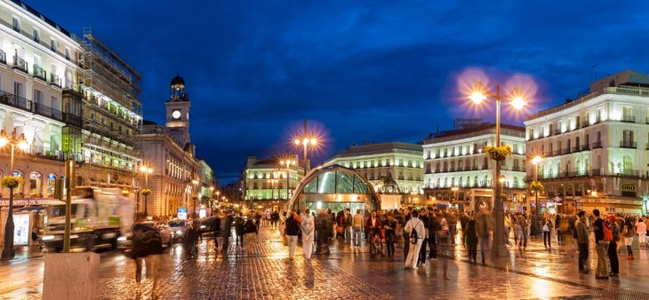 Puerta del Sol de Madrid iluminada al anochecer, con gente paseando entre sus edificios históricos.