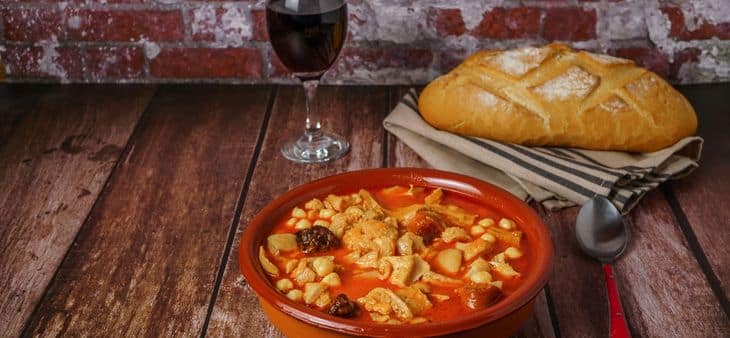 Plato de callos a la madrileña servido en cazuela de barro, acompañado de pan y una copa de vino tinto.