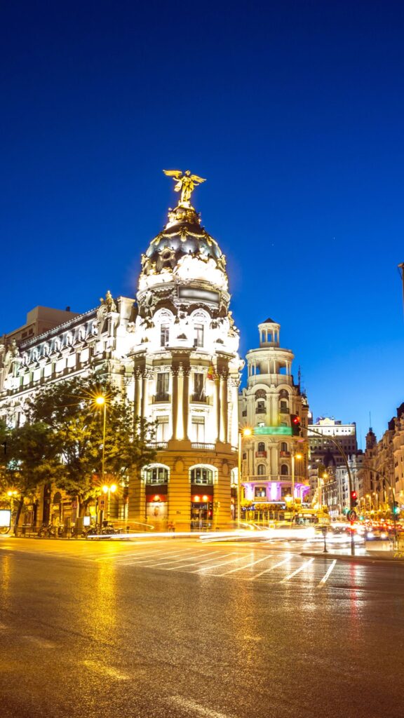 Edificio Metrópolis iluminado por la noche en la Gran Vía de Madrid bajo un cielo azul profundo.