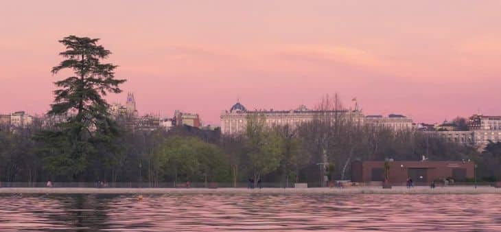 Vista del lago de la Casa de Campo de Madrid al atardecer, con el Palacio Real y la Catedral de la Almudena al fondo.