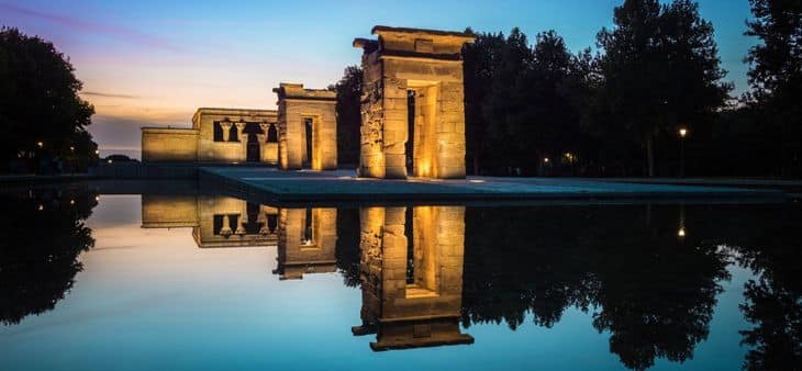 Templo de Debod de Madrid al atardecer, reflejado en el estanque y rodeado de árboles.