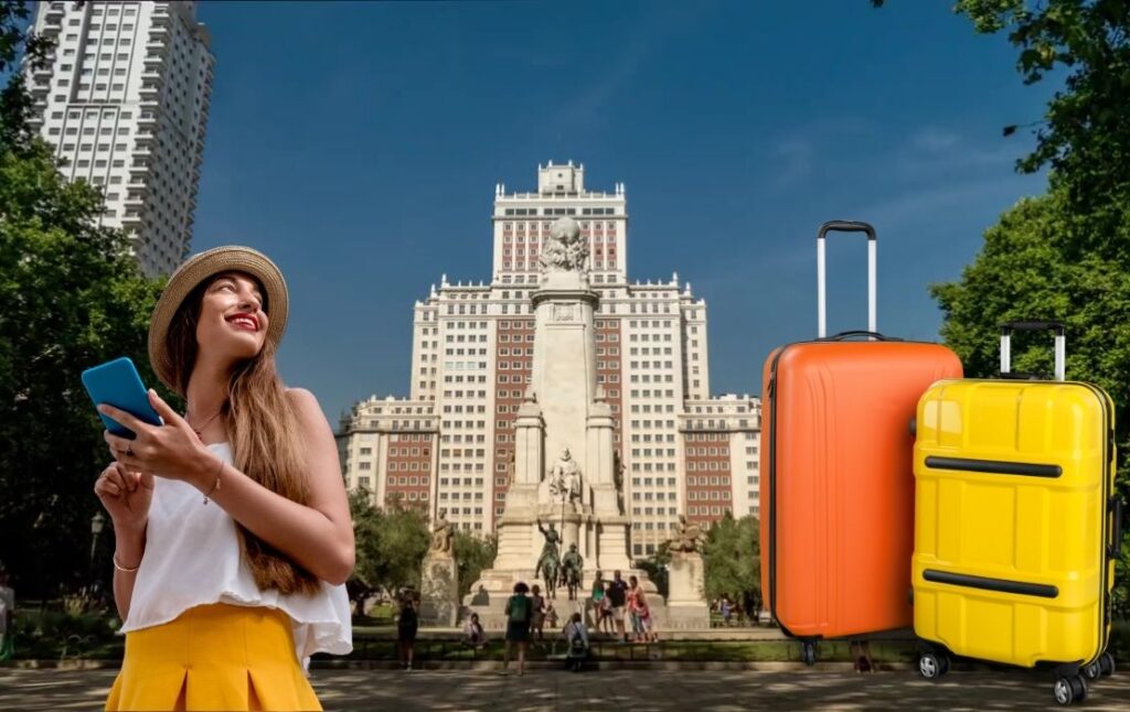 Turista con móvil y maletas frente al Monumento a Cervantes en la Plaza de España de Madrid.