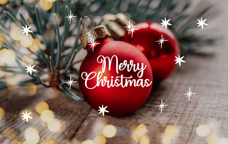 Bola de Navidad roja con mensaje Merry Christmas sobre fondo de madera y luces cálidas.