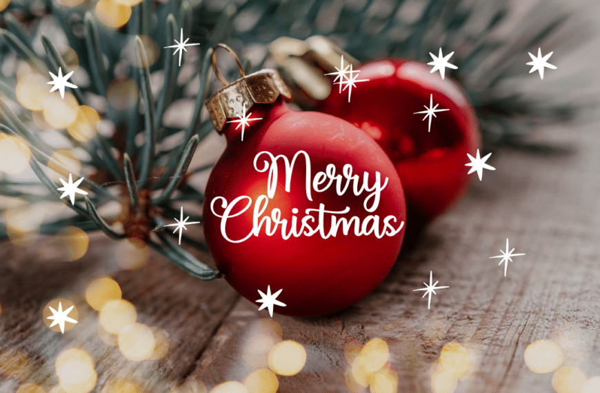 Bola de Navidad roja con mensaje Merry Christmas sobre fondo de madera y luces cálidas.