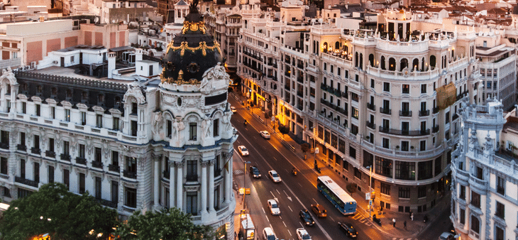 Vista aérea de la Gran Vía de Madrid con edificios históricos y tráfico al atardecer.